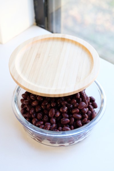 Black beans being stored in a glass bowl with a lid.